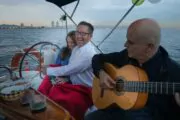 Couple laughing on board a boat while man plays the guitar at sunset
