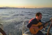 Man playing guitar on the back of a yacht at sunset in Barcelona